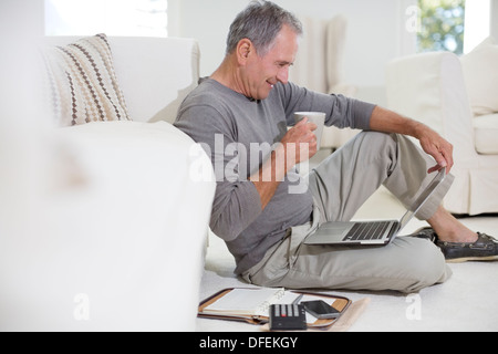 Ältere Mann mit Laptop am Boden des Wohnzimmers Stockfoto