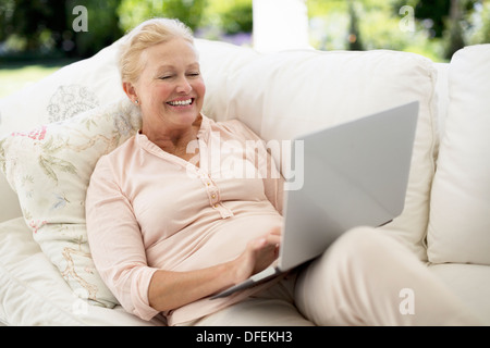 Ältere Frau mit Laptop auf sofa Stockfoto