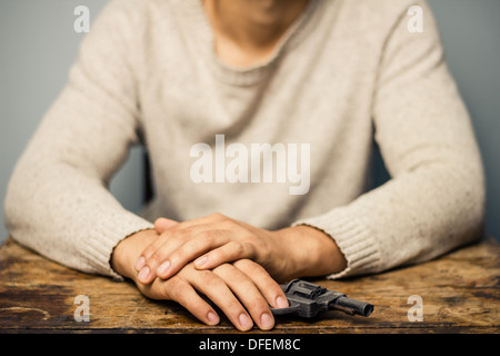 Junger Mann sitzt an einem Tisch mit einem Revolver in der hand Stockfoto