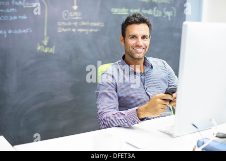 Geschäftsmann mit Handy am Schreibtisch im Büro Stockfoto