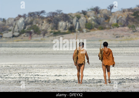 San Bushman Tracker zu Fuß über die gebrochene Pfanne in Richtung der alten Granit Felsvorsprung Kubu Island (Lekhubu), Makgadikgadi Pan, Botswana Stockfoto