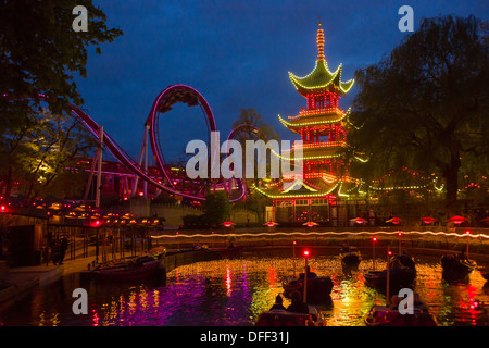 See mit Booten vor dem beleuchteten chinesische Pagode und Achterbahn bei Nacht, Tivoli Gärten, Kopenhagen, Dänemark Stockfoto