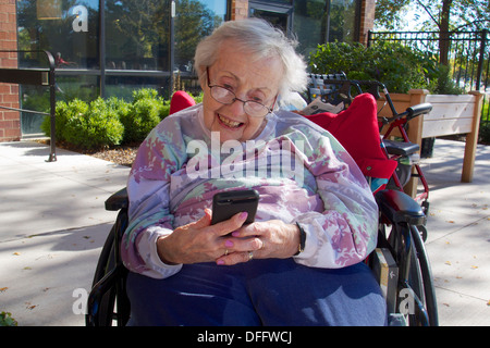 Ältere Frau im Rollstuhl auf Bildschirm des iPhone, lächelnd. Stockfoto