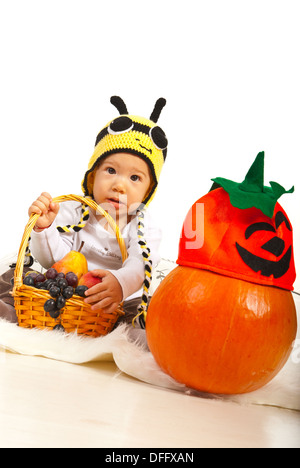 Erstaunt Baby Bee Hut hält Korb mit Trauben und Birnen und sitzen auf Pelz Decke in der Nähe von Kürbis zu Halloween Hut Stockfoto