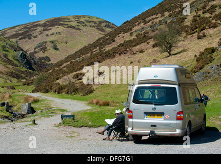 Ein Mann sitzt mit einem Wohnmobil auf einem Parkplatz in Carding Mill Valley, Long Mynd, Kirche Stretton, Shropshire, England Stockfoto