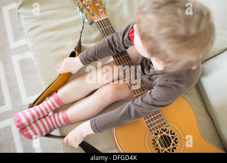 Junges Mädchen, 4 Jahre alt, sitzt im Sofa mit Akustik-Gitarre Stockfoto