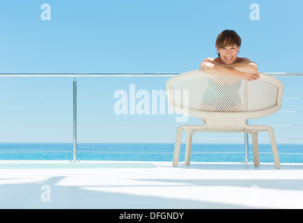 Porträt der lächelnde Frau in Stuhl auf der Terrasse mit Blick auf Meer Stockfoto