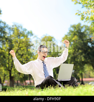 Junger Mann, jubeln und vor dem Fernseher auf einem Laptop in einem Park an einem sonnigen Tag Stockfoto