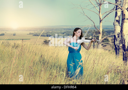 Junge schöne Frau im dunklen Cyan Kleid beim Musizieren auf weiße Geige Stockfoto