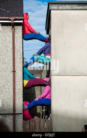 Bangor, Wales, UK. 5. Okt, erstellen 2013,20 bunt gekleidete junge Interpreten bunte statische Bilder, wie sie ihren Körper in Räume und Hohlräume in der Stadt Bangor in Nordwales einfügen. Österreichische Choreograf WILLI DORNER ersonnen, ist "Einrichtungen im urbanen Raum" eine weltweite Reisen Performance mit lokalen Tänzer und Turner. gequetscht und ausgewogen unter Architektur der Stadt. Hunderte von Menschen folgten ihren Fortschritt durch die Stadt auf eine einstündige kostenlose Leistung. Bildnachweis: Keith Morris/Alamy Live-Nachrichten Stockfoto