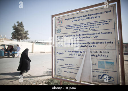 Kunduz, Afghanistan. 5. Oktober 2013. Eine Frau geht vorbei an einem verwitterten Zeichen, das bezieht sich auf die Finanzierung einer Straße durch die Bundesrepublik Deutschland in Kunduz, Afghanistan, 5. Oktober 2013. Die 1,15 km lange wurde mit Hilfe des BMZ (Bundesministerium für wirtschaftliche Zusammenarbeit) und KfW (Kreditanstalt) Straße gebaut. Soldaten der deutschen Kontingenz des International Sicherheit Assistance Force (ISAF) am 06 Oktober zog sich schließlich aus ihrer Basis in Kunduz, die von nun an von der afghanischen Armee (ANA) und die ANCOP verwendet werden. Foto: MICHAEL KAPPELER/Dpa/Alamy Liv... Stockfoto