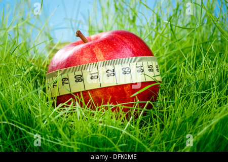 Roter Apfel und ein Maßband auf dem grünen Rasen. Stockfoto