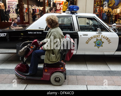 Eine senior Lady in eine mobile Mobilität fährt vorbei an einem Polizeiauto California Highway Patrol Stockfoto