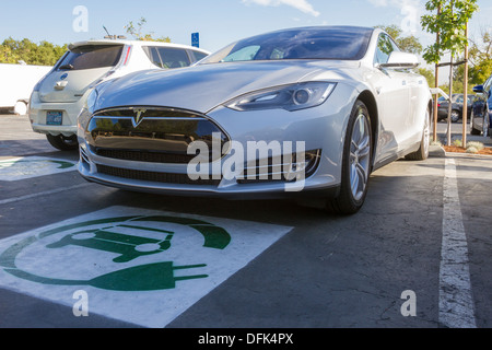 Tesla Model S Plug-in-Elektro-Auto geparkt in eine Parklücke mit EV-Symbol und eine Ladestation am Arbeitsplatz angeschlossen Stockfoto