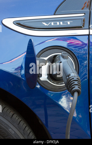 Chevrolet Volt Plug-in-Elektro-Fahrzeug mit Stecker eingesteckt und mit Reflexion der amerikanischen Flagge auf dem Auto aufladen Stockfoto