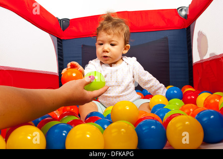 Mutter Aushaendigen bunte Bällen zu sein kleiner Sohn im Laufstall Stockfoto