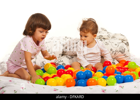Kleine Mädchen und Baby Junge sitzt auf dem Bett und spielt mit bunten Kugeln Stockfoto