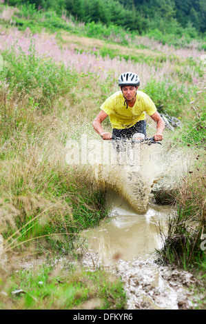 Ein junger Mann auf dem Mountainbike, Reiten durch eine schlammige Pfütze in Graslandschaft Stockfoto