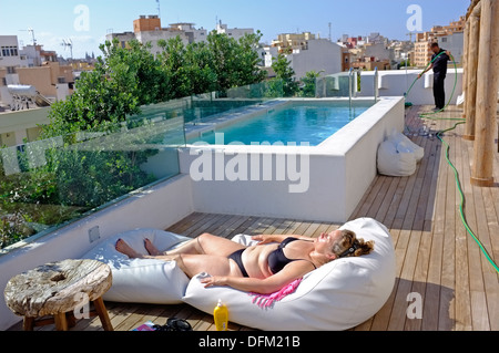 Ein weiblicher Touristen liegt in der Sonne auf einem Hoteldach, während ein Mann reinigt. Palma De Mallorca Stockfoto