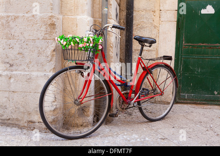 Altes Fahrrad mit Korb, dekoriert mit Blumen gegen eine Steinmauer Stockfoto