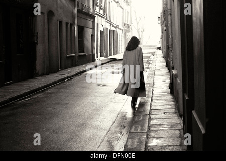 Elegante Dame, die zu Fuß entlang der feuchten Straße in den frühen Morgenstunden auf der Île Saint Louis in Paris Stockfoto