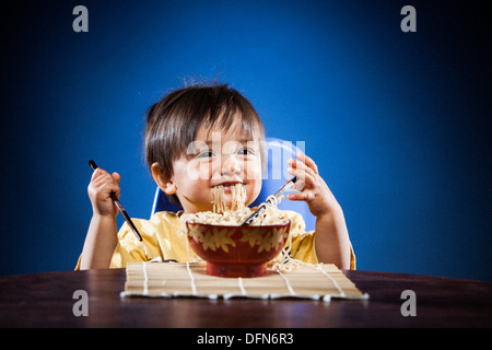 Eine 16 Monate alte, Japanisch-amerikanischer Junge isst Ramen-Nudeln mit Stäbchen auf eine Bambus-Matte. Stockfoto