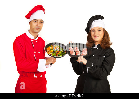 Köche zeigen Bratpfannen mit Gemüse und Fleisch Stockfoto