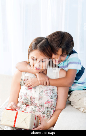 Junge umarmt seine Mutter von hinten hält ein Geschenk Stockfoto