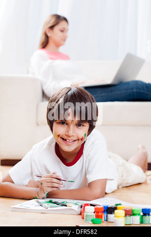 Junge, ein Gemälde mit seiner Mutter mit Laptop im Hintergrund Stockfoto