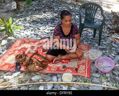 Kosrae Frau sitzt auf einer Strohmatte am Rande des Ozeans, während sie getrockneten Palmwedeln und Muscheln in Wand Hangings verwebt Stockfoto