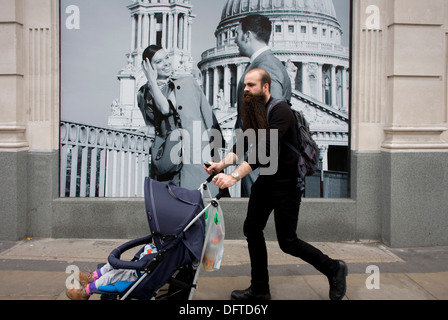 Ein Mann schiebt ein Kind Buggy vorbei ein Mode-Plakat zeigt einen Mode-jungen und Mädchen und St. Pauls Cathedral. Stockfoto