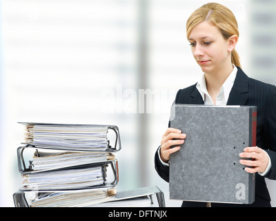 Nachdenkliche junge Geschäftsfrau vor einem Haufen von Ordnern Stockfoto