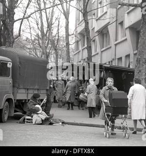 Menschen gehen auf einem Wochenmarkt einkaufen, während Behinderte Banjo-Spieler am Straßenrand in das Viertel Montmartre in Paris, Frankreich, im November 1970 sitzt. Foto: Wilfried Glienke Stockfoto