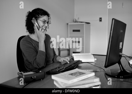 Nicole, Doktorand am Telefon spricht und lächelt, während sie in ihrem Büro an einer Aufgabe arbeitet. Stockfoto