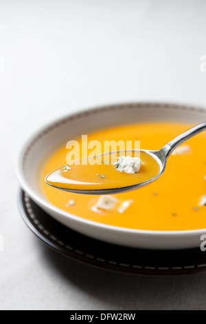 Creme von Kürbissuppe mit Blauschimmelkäse auf einem Löffel mit der Schüssel im Hintergrund. Stockfoto