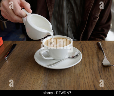 Man gießt Milch in Kaffee. Stockfoto