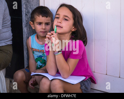 Portugal Algarve Loule Markt zwei süße Brünette junge Kinder Jungen Mädchen sitzen Tür grün Kugelschreiber Übungsbuch nachdenklicher Blick lange Haare Stockfoto