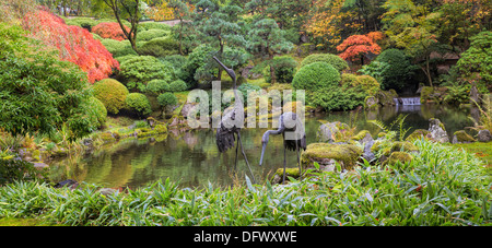 Japanische Bronze Krane Skulptur paar Wasser Teich mit Bäume Pflanzen und Sträucher im Herbst Panorama Stockfoto