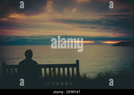 Ein Mann saß auf einer Bank, Blick auf den Sonnenuntergang über dem Meer Stockfoto