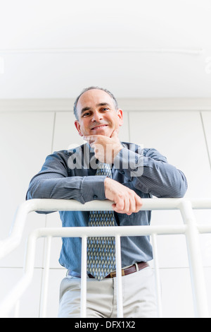 Lächelt stolz Geschäftsmann im Büro Flur stützte sich auf Geländer Schuss von unten stehend Stockfoto