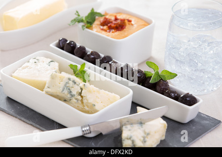 Vorspeisen-Blauschimmelkäse und schwarz marinierte Oliven auf dem Schiefer Käse Schneidebrett mit Eiswasser und Hummus Stockfoto