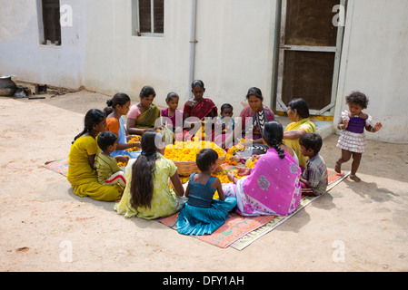 Ländliche Indianerdorf Frauen und Kinder sitzen rund um einen Korb mit Ringelblumen machen Blumengirlanden. Andhra Pradesh, Indien Stockfoto