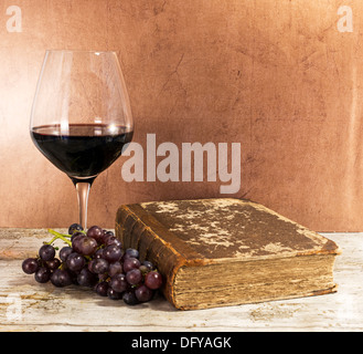 altes Buch und Rotwein mit Trauben auf Tisch Stockfoto