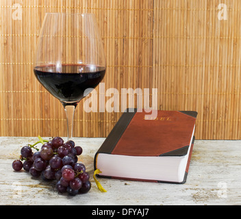 alte Bibel und Rotwein mit Trauben auf Tisch Stockfoto