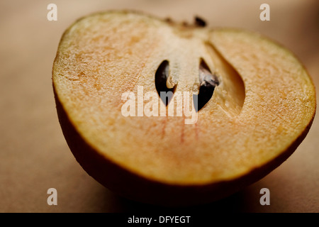 Sapodilla. Eine frisch geschnittene Hälfte der Frucht befindet sich auf braunem Hintergrund Stockfoto