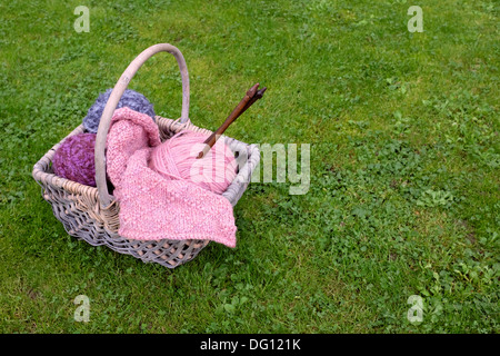 Geflochtenen Korb mit Stricken, hölzerne Nadeln und weiches Garn auf dem grünen Rasen Stockfoto