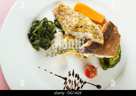 Fischgericht mit Spinat, eine Auswahl von Fischfilets auf einer Platte, mit Gemüse und Kräutern garniert serviert Stockfoto
