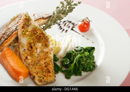 Fischgericht mit Spinat, eine Auswahl von Fischfilets auf einer Platte, mit Gemüse und Kräutern garniert serviert Stockfoto