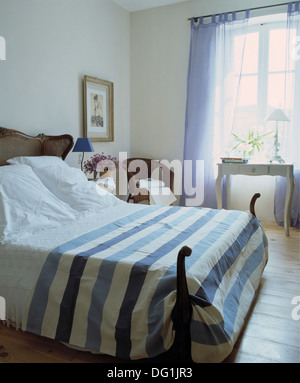 Blau + weiß gestreiften Bettdecke und Kissen auf antikes Bett im französischen Schlafzimmer mit lackierten Parkettboden und blaue Vorhänge Stockfoto