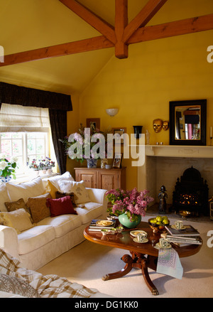 Weißes Sofa und niedrige, Runde Couchtisch in gelb Wohnzimmer Erweiterung mit Holzbalken Apex Decke und Spiegel über dem Kamin Stockfoto